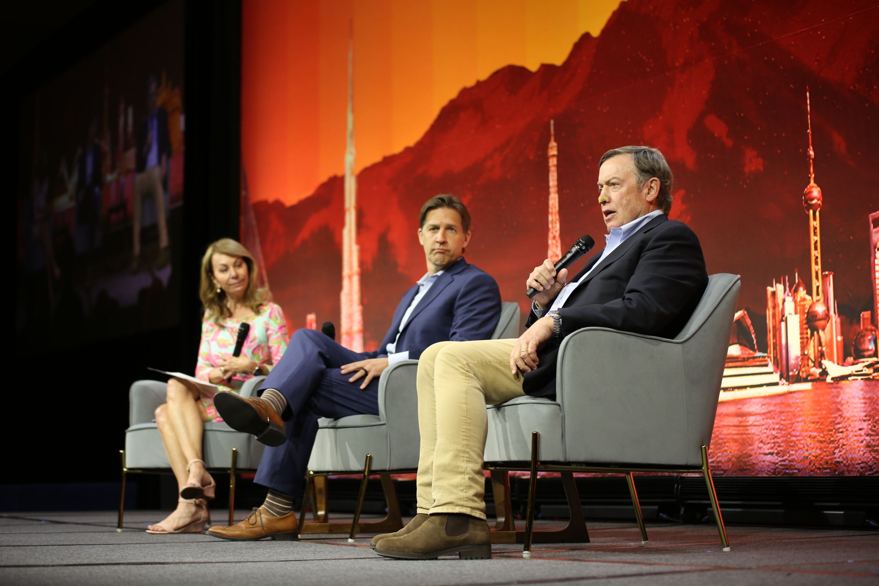 Three people sit on stage holding microphones and discussing the role of universities during a large educational technology conference.  