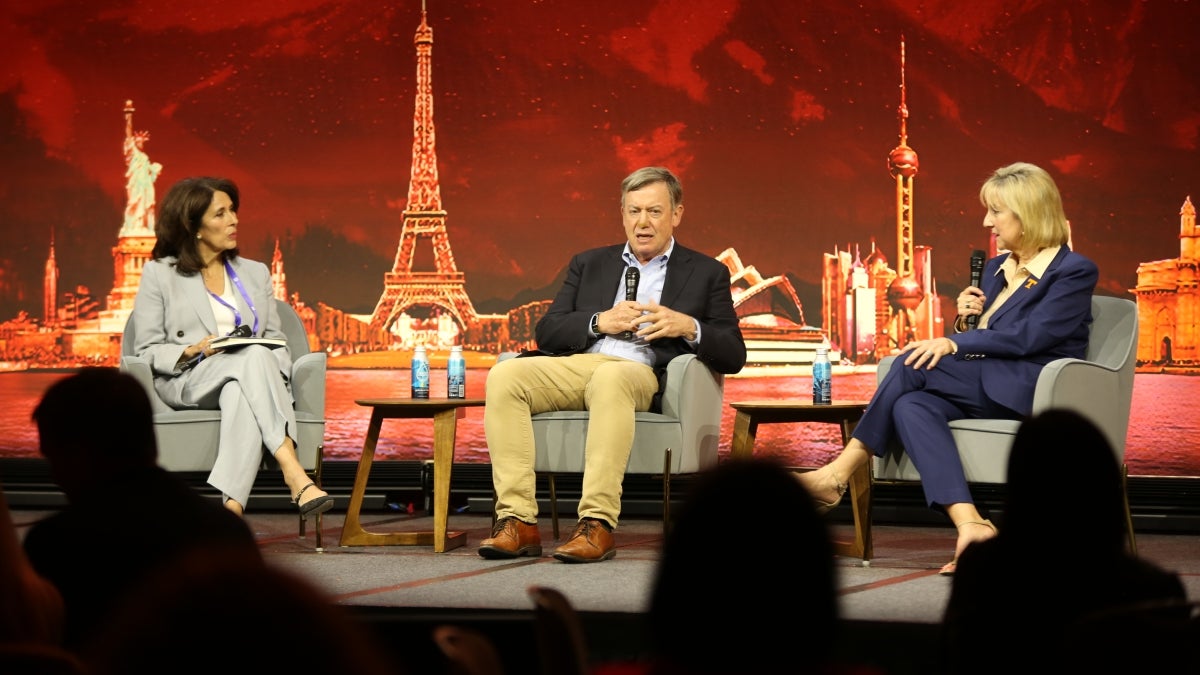 Three people sit on on-stage discussing the need for collaboration in higher education. 