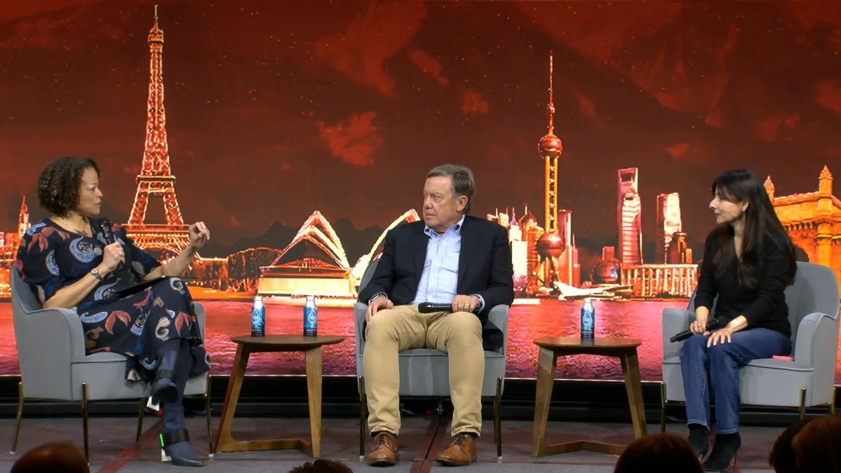 Three people sit on stage in front of a backdrop illustrated with global landmarks to discuss global access to education using edtech. 
