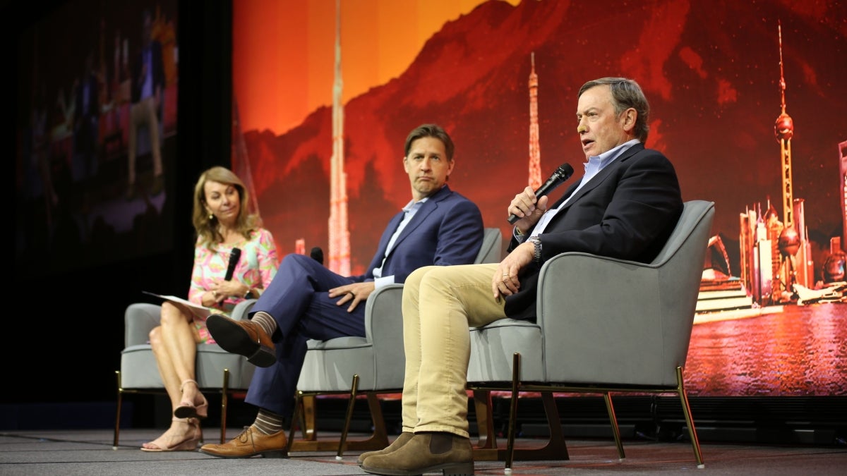 Three people sit on stage holding microphones and discussing the role of universities during a large educational technology conference. 