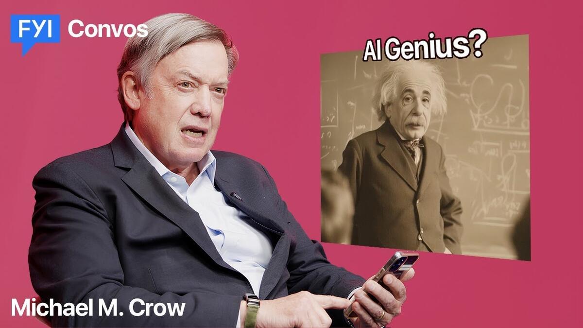 A person in a white shirt and dark suit jacket holds a cell phone in his hand while answering questions about the power of AI, in front of a photo Albert Einstein.