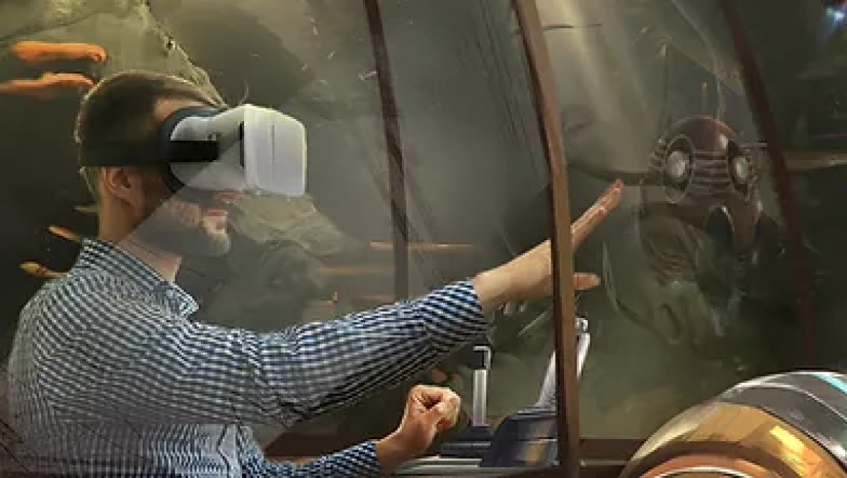 A person with short hair in a plaid long-sleeve shirt wears a virtual reality headset and reaches a right hand forward to touch an object. 