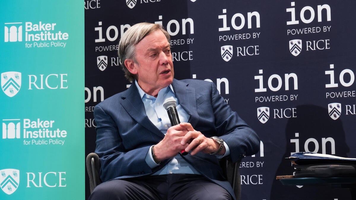 A person in business attire sits and speaks into a microphone on-stage during a fireside chat about US research universities. 