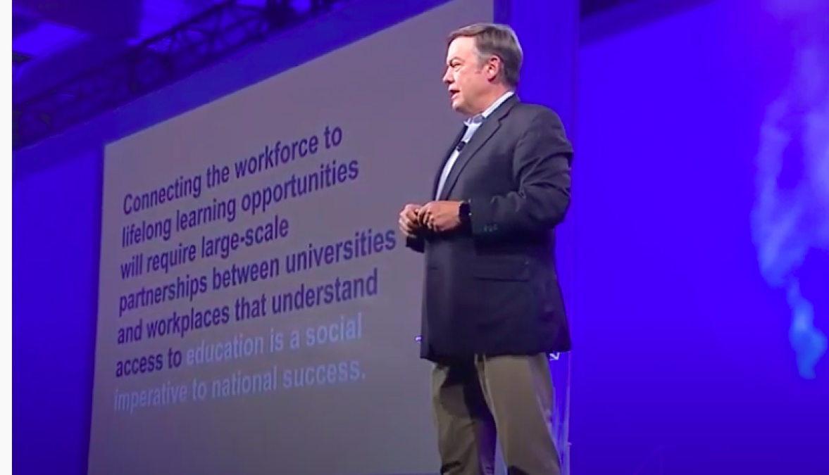 A middle-aged man in beige slacks and a blue jackets stands on a stage in front of a PowerPoint slide at the 2019 ASU GSV Summit. 