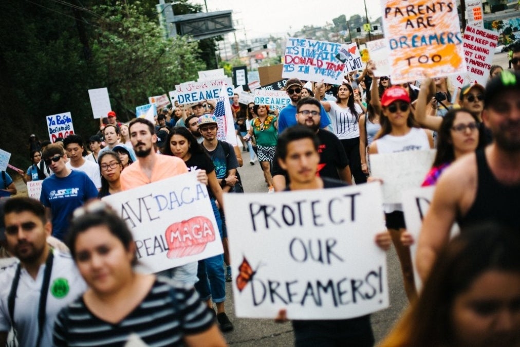 A large group of people march on a street holding handmade signs in support of the Dream Act and students. 