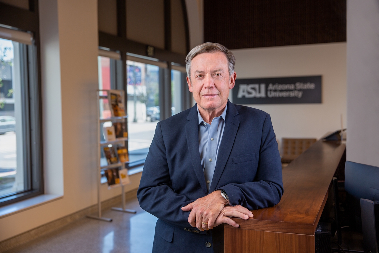 A person wearing a blue blazer and shirt leans on a reception desk in the ASU California Center lobby.